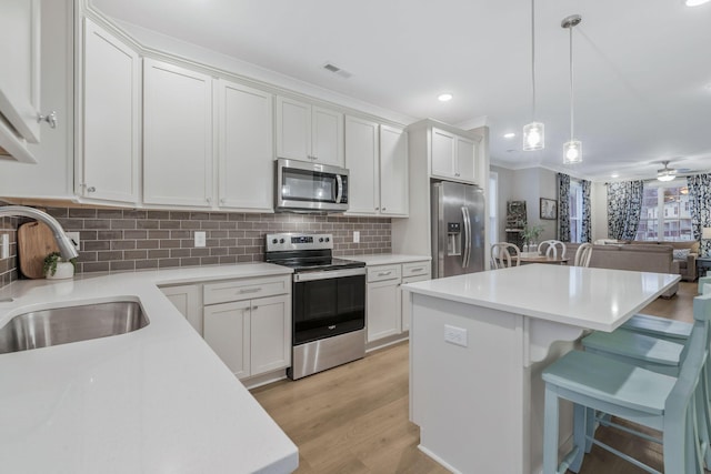 kitchen with decorative backsplash, light wood-style flooring, a kitchen breakfast bar, stainless steel appliances, and a sink