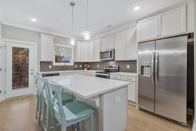 kitchen featuring a sink, appliances with stainless steel finishes, a kitchen bar, crown molding, and tasteful backsplash