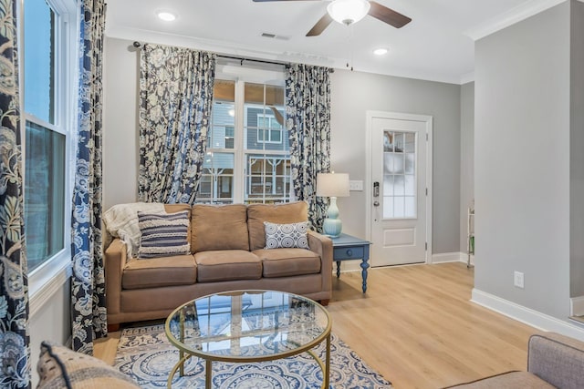 living area with visible vents, crown molding, baseboards, wood finished floors, and a ceiling fan