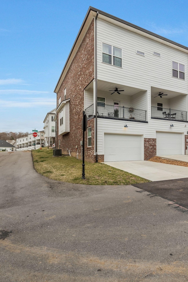 view of property featuring driveway, a ceiling fan, a balcony, a front yard, and brick siding