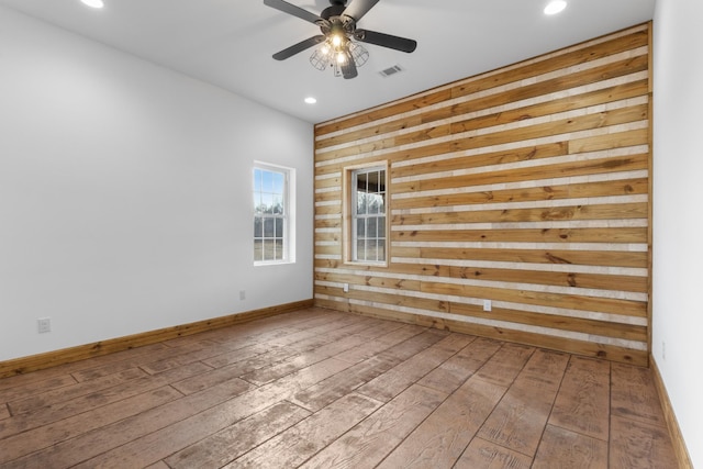 unfurnished room with visible vents, wood walls, ceiling fan, and hardwood / wood-style flooring