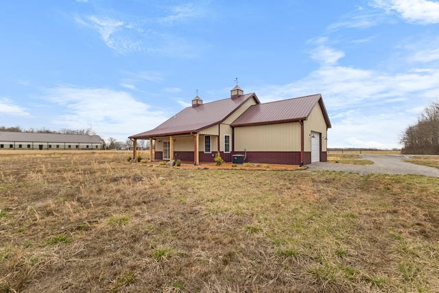 back of house with central air condition unit, a chimney, a garage, and metal roof