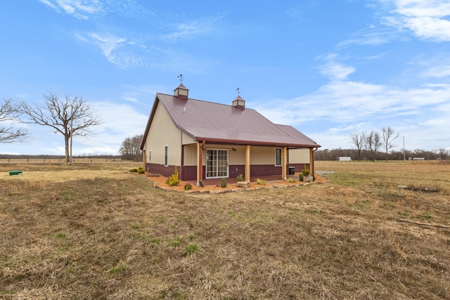 exterior space featuring a porch, a chimney, a rural view, a lawn, and metal roof