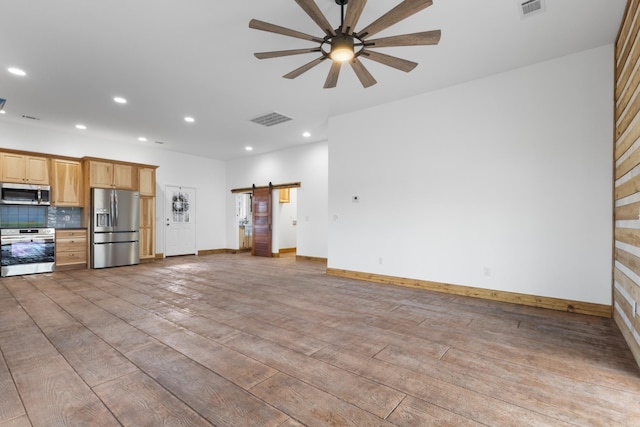 unfurnished living room with a barn door, visible vents, light wood-style flooring, and a ceiling fan