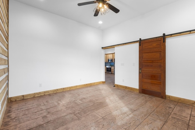 spare room featuring ceiling fan, baseboards, a barn door, and wood finished floors