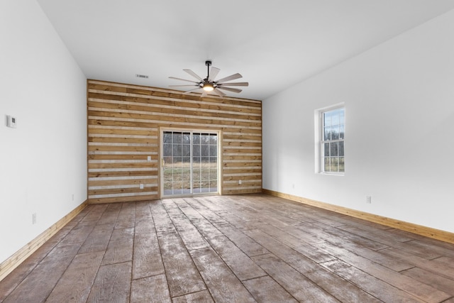 empty room featuring hardwood / wood-style floors, a ceiling fan, visible vents, baseboards, and wood walls