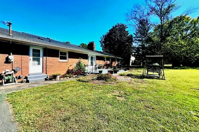 rear view of property featuring brick siding, a lawn, and entry steps