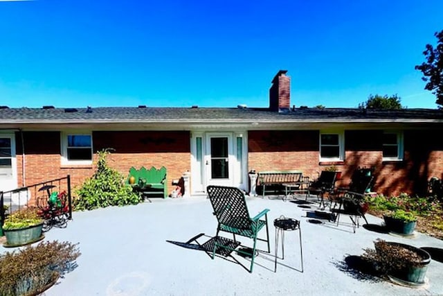 back of house featuring brick siding, a chimney, and a patio