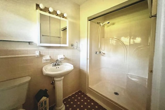 bathroom featuring a shower stall, toilet, tile walls, and wainscoting