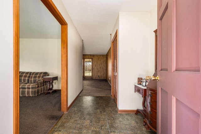 hall with stone finish flooring, baseboards, and dark colored carpet