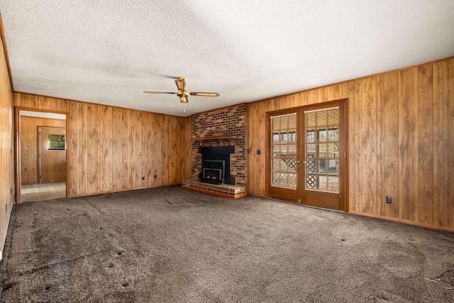 unfurnished living room featuring ceiling fan, carpet, wood walls, and a textured ceiling