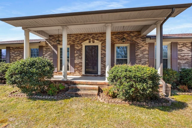 entrance to property featuring a porch, a lawn, and brick siding