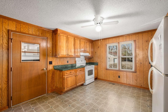kitchen featuring under cabinet range hood, white appliances, light floors, and wood walls