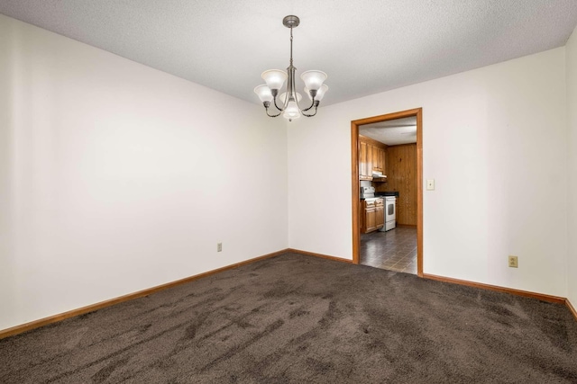 spare room featuring a chandelier, a textured ceiling, baseboards, and dark colored carpet