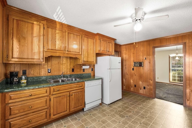 kitchen with a sink, white appliances, dark countertops, and wood walls