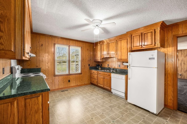 kitchen with brown cabinetry, wooden walls, white appliances, and dark countertops