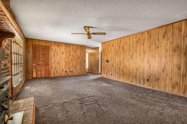 carpeted spare room featuring wooden walls, a ceiling fan, and a textured ceiling