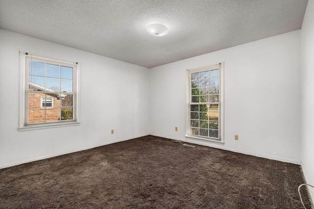 unfurnished room with a textured ceiling and dark colored carpet