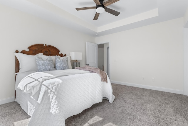 bedroom featuring a tray ceiling, carpet floors, baseboards, and ceiling fan