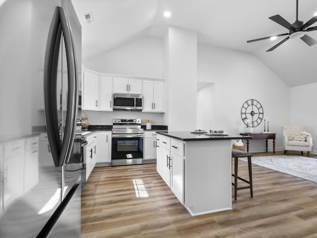 kitchen with a kitchen island, stainless steel appliances, light wood-style floors, dark countertops, and a kitchen breakfast bar