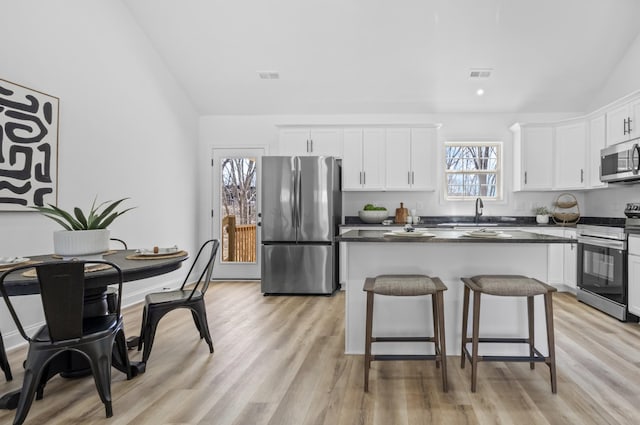 kitchen featuring visible vents, a center island, white cabinetry, stainless steel appliances, and lofted ceiling