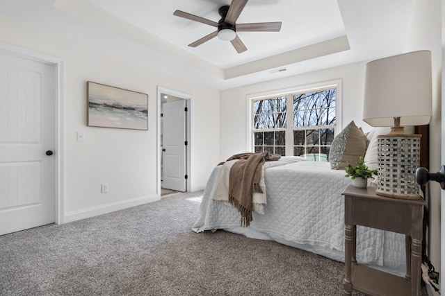 carpeted bedroom featuring baseboards, a raised ceiling, visible vents, and ceiling fan