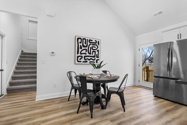 dining area with visible vents, high vaulted ceiling, stairway, light wood-style floors, and baseboards