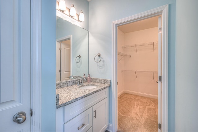 bathroom with a walk in closet, baseboards, and vanity