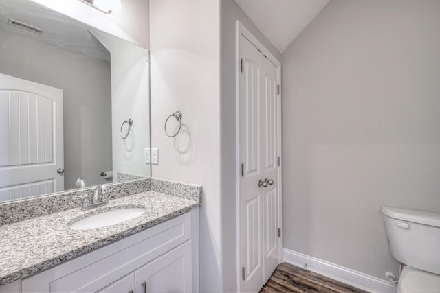 bathroom featuring visible vents, toilet, wood finished floors, baseboards, and vaulted ceiling