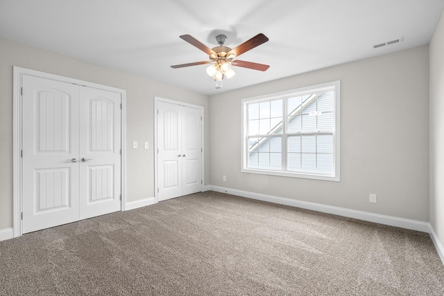 unfurnished bedroom featuring baseboards, visible vents, carpet floors, ceiling fan, and two closets