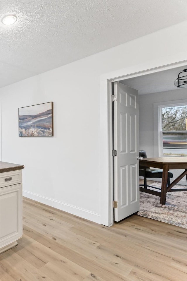 dining area with baseboards, light wood-style floors, and a textured ceiling