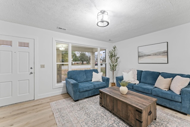 living room featuring light wood finished floors, visible vents, and a textured ceiling