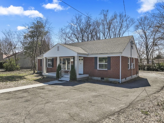 bungalow-style house featuring brick siding, covered porch, aphalt driveway, and roof with shingles