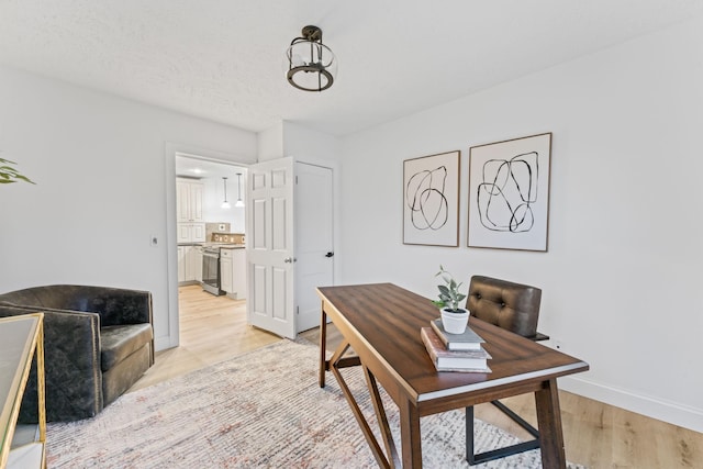 office area with light wood finished floors, a textured ceiling, and baseboards