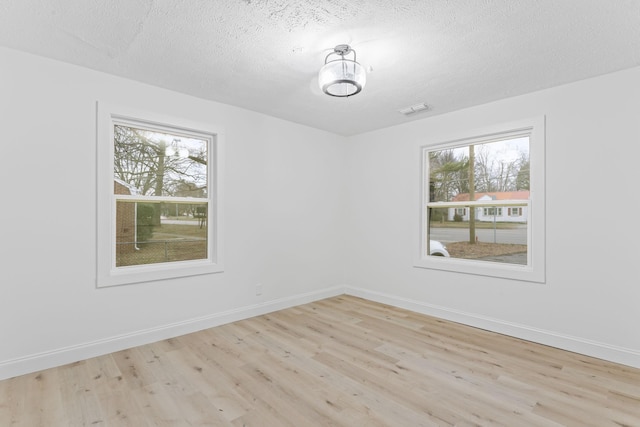 unfurnished room featuring baseboards, wood finished floors, visible vents, and a textured ceiling