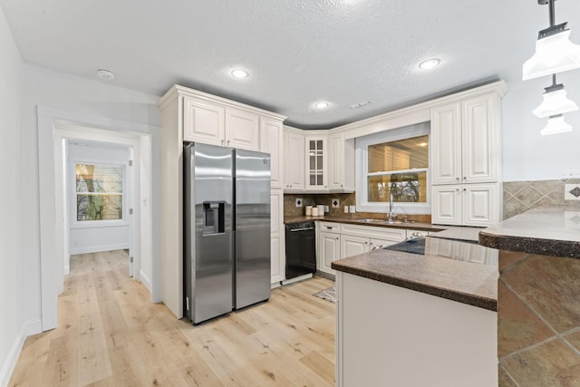 kitchen featuring dark countertops, tasteful backsplash, light wood-style flooring, stainless steel fridge, and a sink