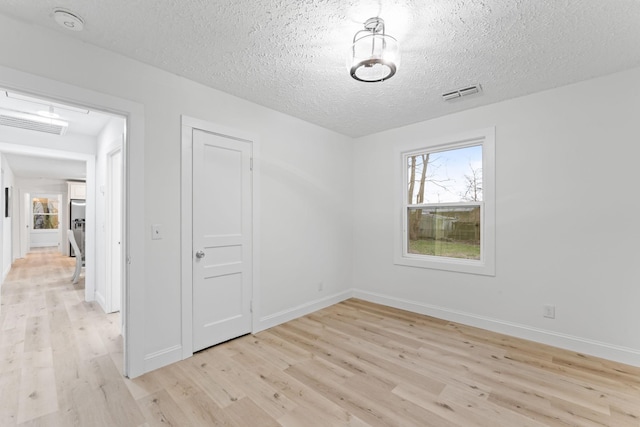 spare room with visible vents, baseboards, light wood-style floors, and a textured ceiling