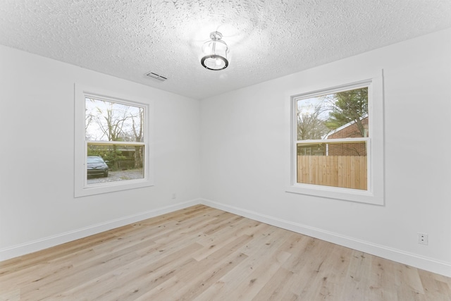 spare room featuring light wood-type flooring, visible vents, baseboards, and a textured ceiling