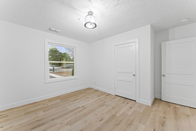 spare room featuring light wood-type flooring, visible vents, baseboards, and a textured ceiling