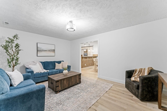 living area with light wood-style flooring, baseboards, visible vents, and a textured ceiling