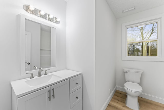 half bathroom featuring baseboards, toilet, vanity, wood finished floors, and a textured ceiling