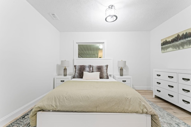 bedroom with light wood finished floors, visible vents, a textured ceiling, and baseboards