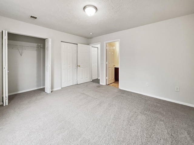 unfurnished bedroom with baseboards, visible vents, multiple closets, a textured ceiling, and carpet flooring