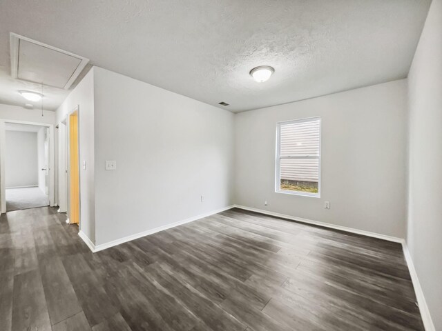 spare room with visible vents, a textured ceiling, dark wood finished floors, baseboards, and attic access