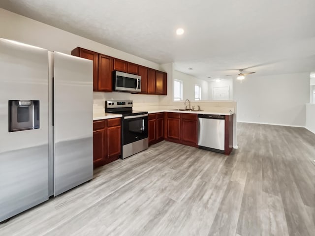 kitchen with a sink, stainless steel appliances, light wood-style floors, a peninsula, and light countertops