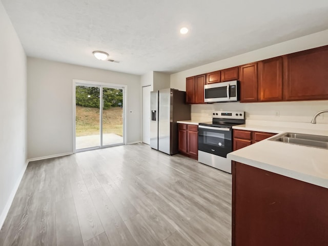 kitchen featuring baseboards, light wood finished floors, a sink, light countertops, and appliances with stainless steel finishes