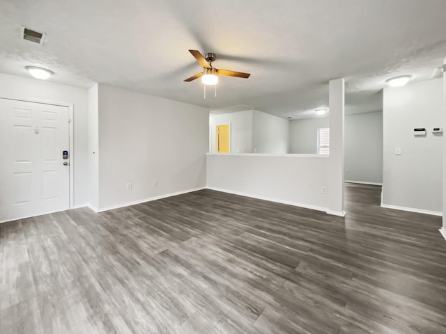 unfurnished living room featuring visible vents, baseboards, dark wood-type flooring, and a ceiling fan