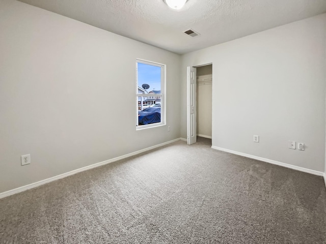 carpeted empty room with baseboards, visible vents, and a textured ceiling