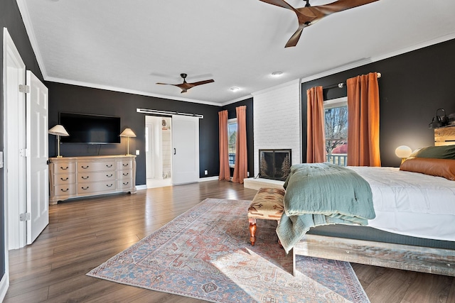 bedroom featuring baseboards, a barn door, ornamental molding, wood finished floors, and a ceiling fan