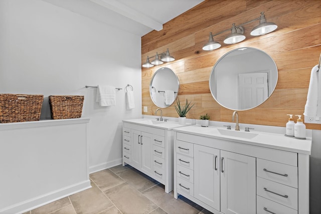 bathroom featuring beam ceiling, wooden walls, two vanities, and a sink